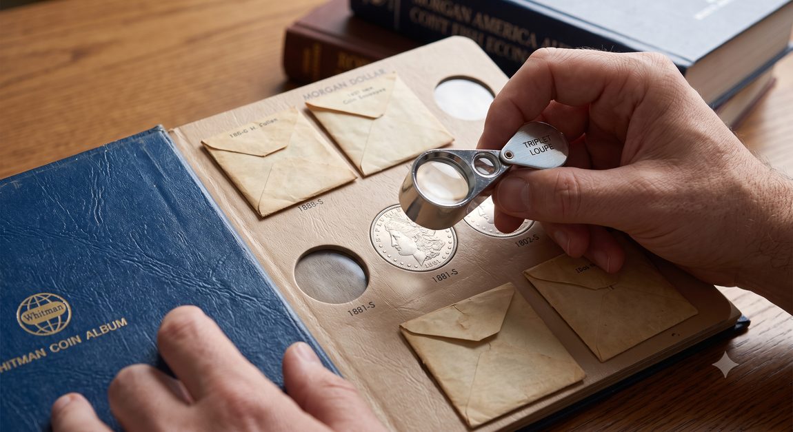 A collector examines a silver Morgan Dollar with a loupe inside a vintage Whitman coin album