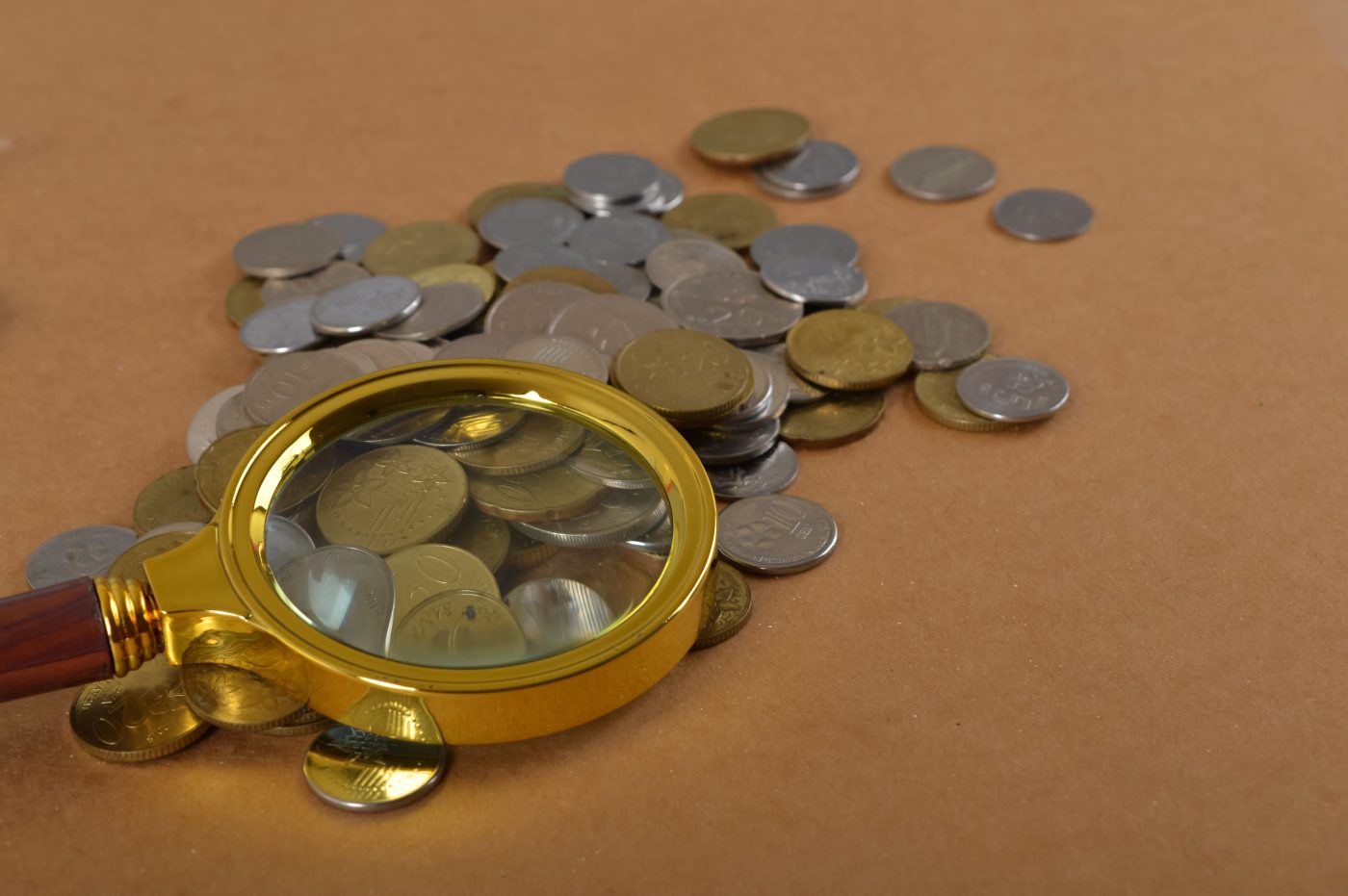 A magnifying glass resting over a pile of world coins