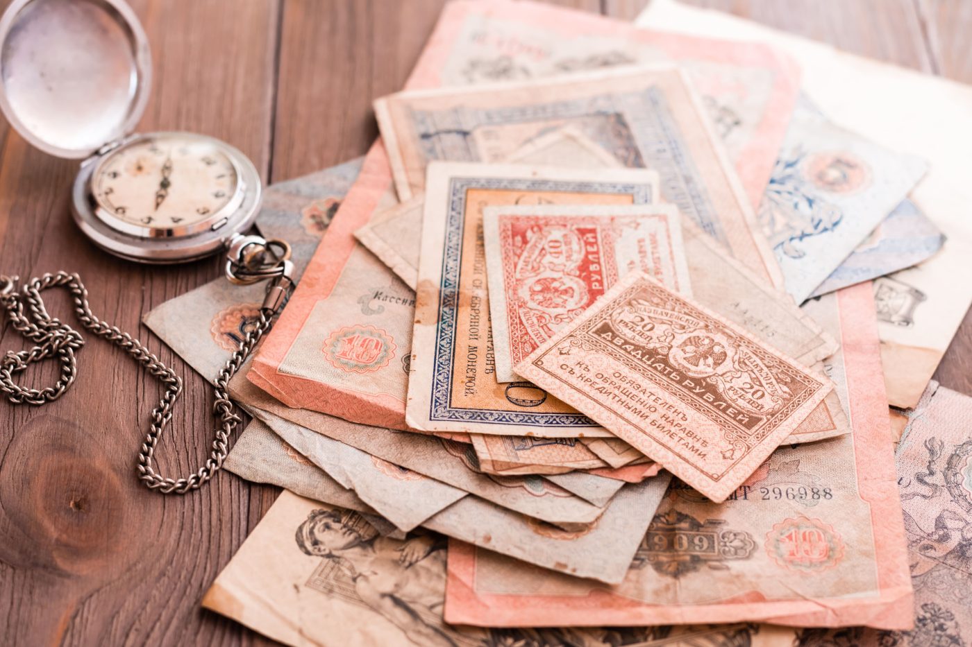 An antique pocket watch resting on a stack of vintage banknotes