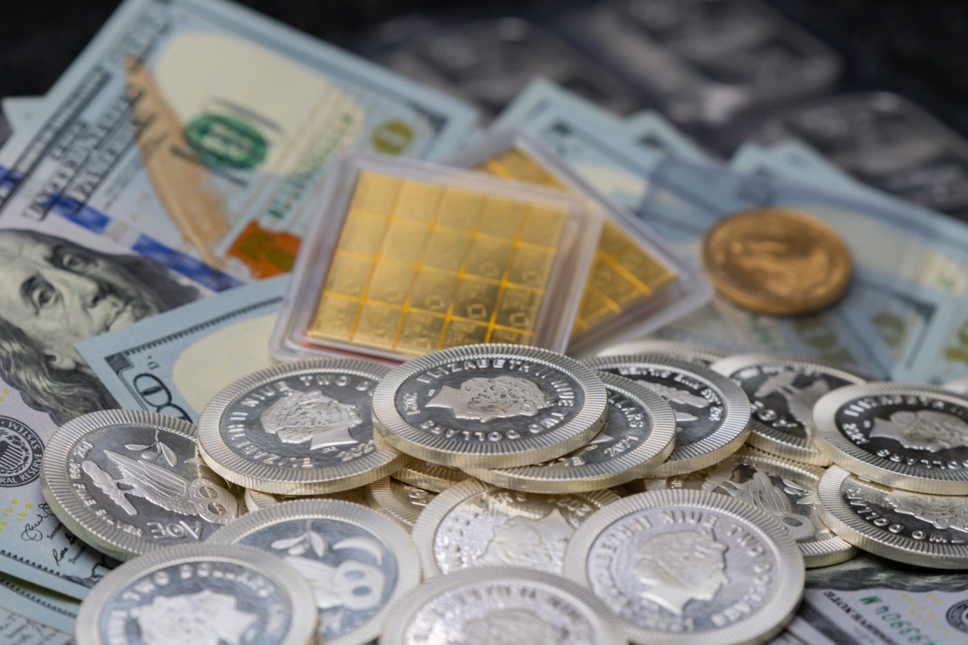 Gold bullion and silver coins stacked on top of dollar bills