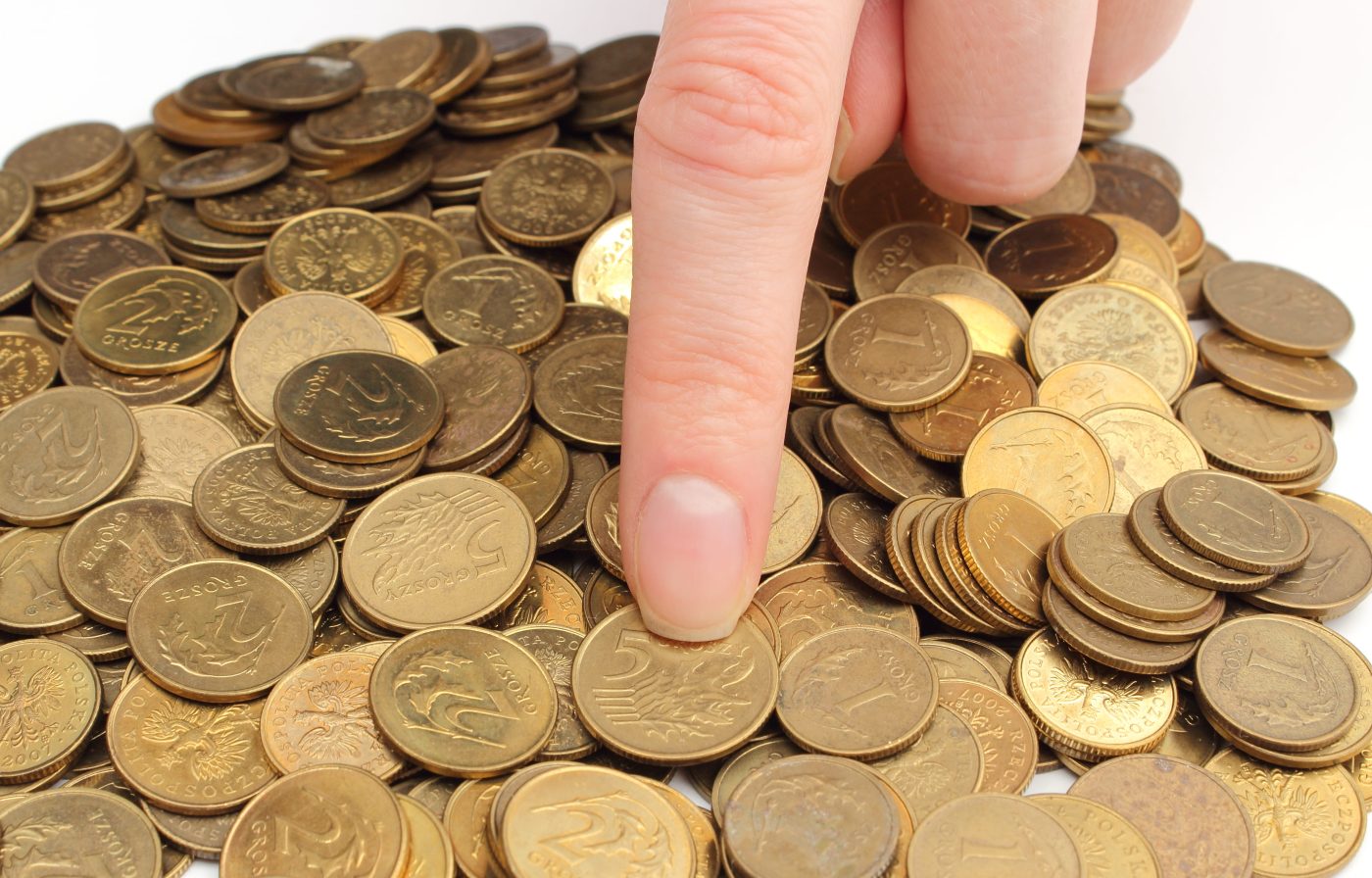 A hand selecting a coin from a large pile of loose coins